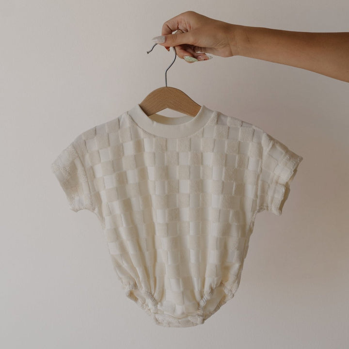 Baby romper on a hanger against a plain background