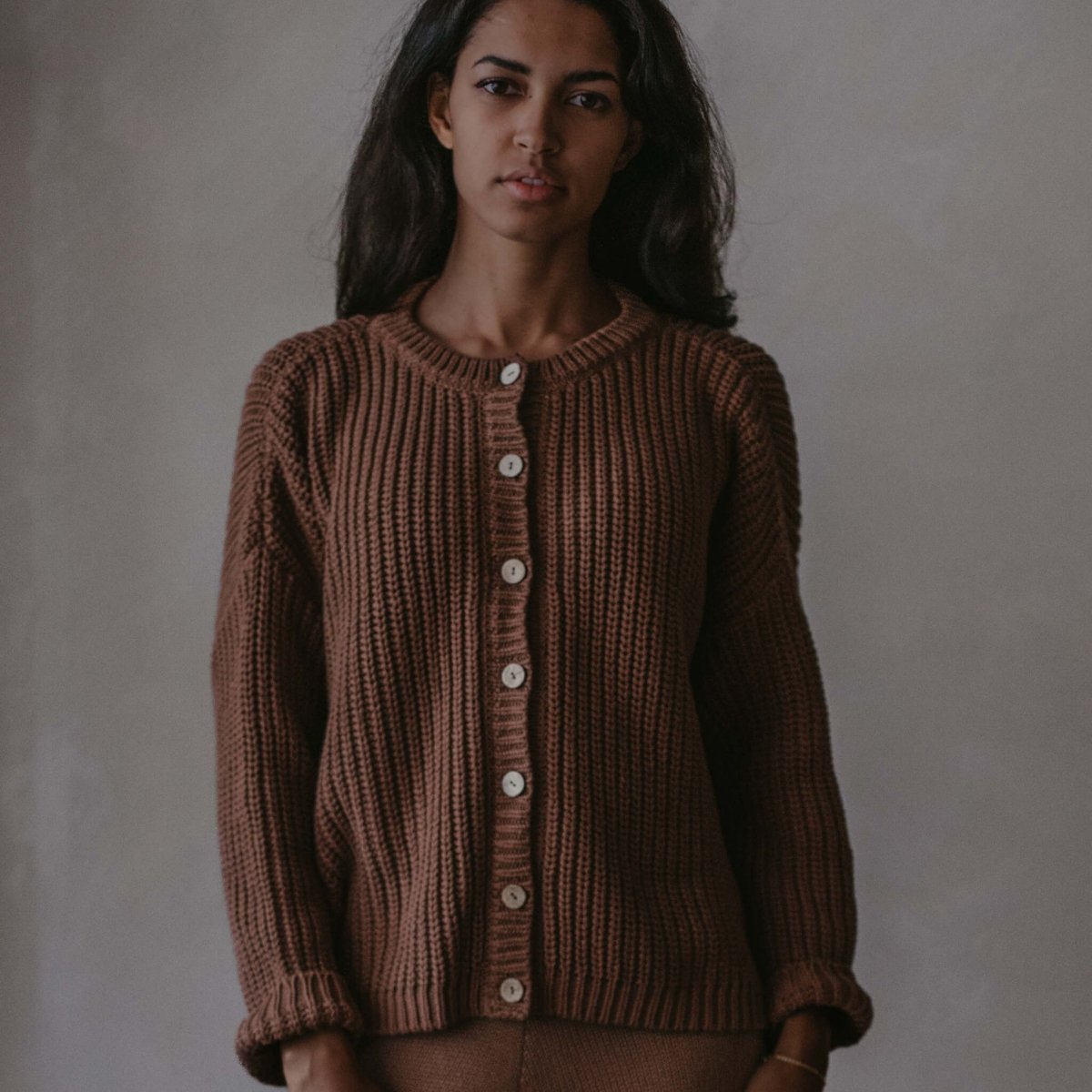 Woman wearing a brown knitted cardigan against a plain background