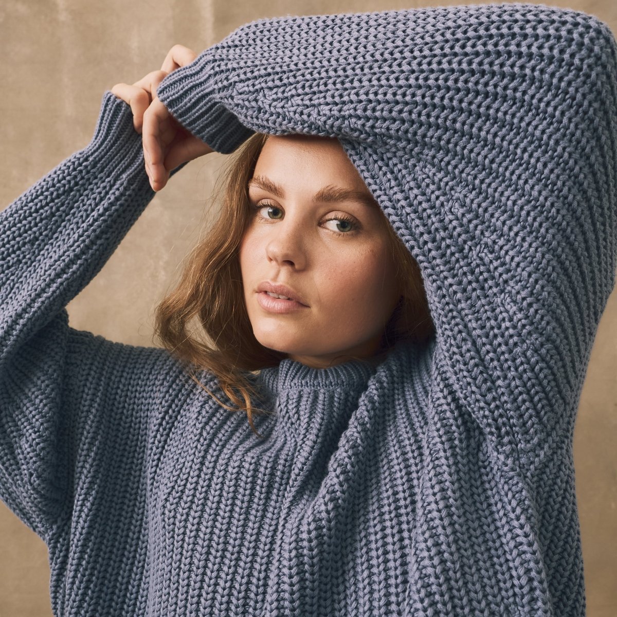 Woman wearing a large blue knitted sweater against a beige background