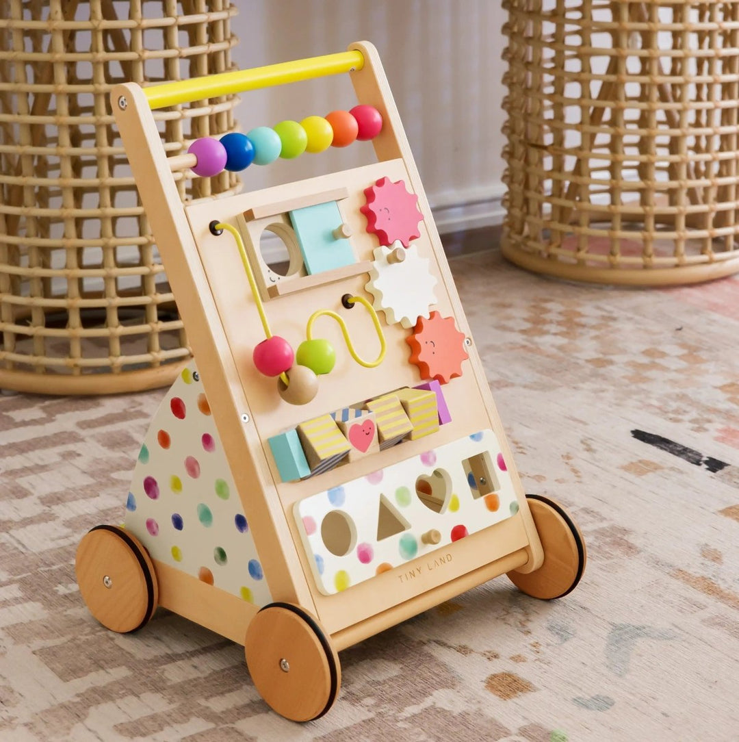 Wooden children's activity toy with colorful beads and shapes on wheels, placed indoors.