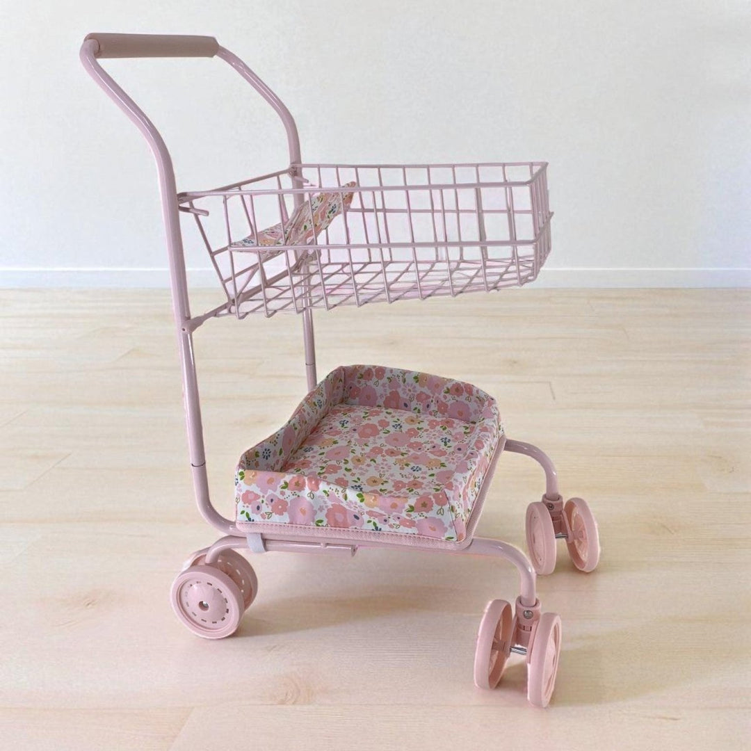 Pink toy shopping cart with floral seat on a light wooden floor