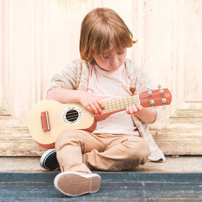 Child playing a ukulele with a wooden background