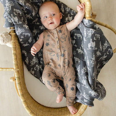 Baby in a woven basket with a dark blanket featuring animal prints