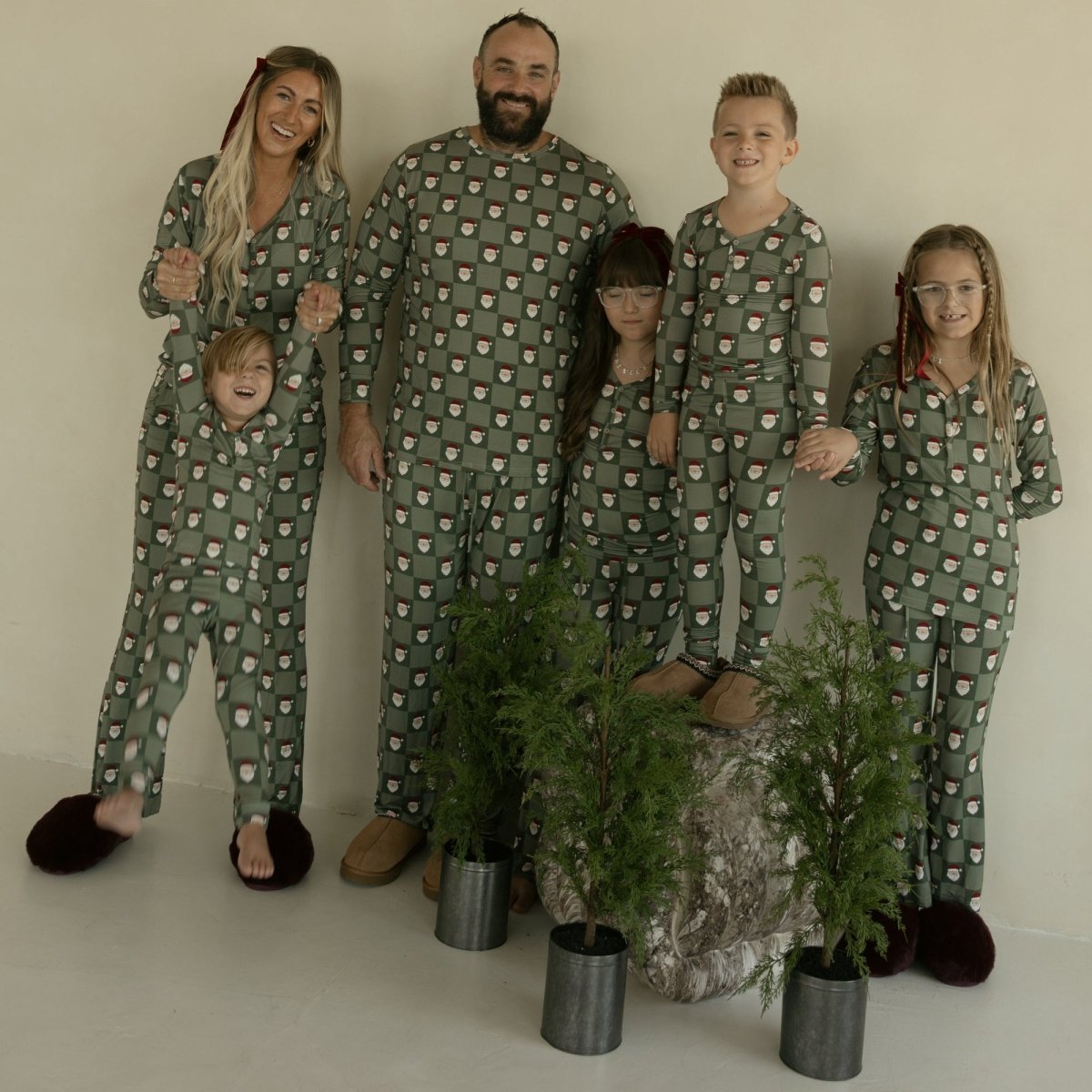 Family of six wearing matching green pajamas with a pattern, standing in front of a plain background.
