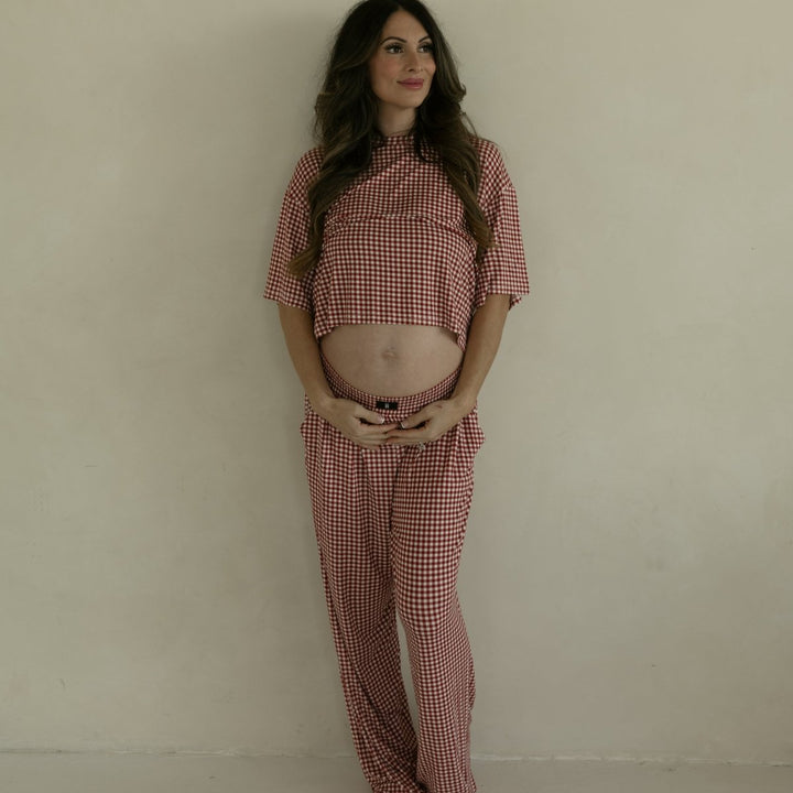 Pregnant woman wearing a red checkered outfit against a plain background
