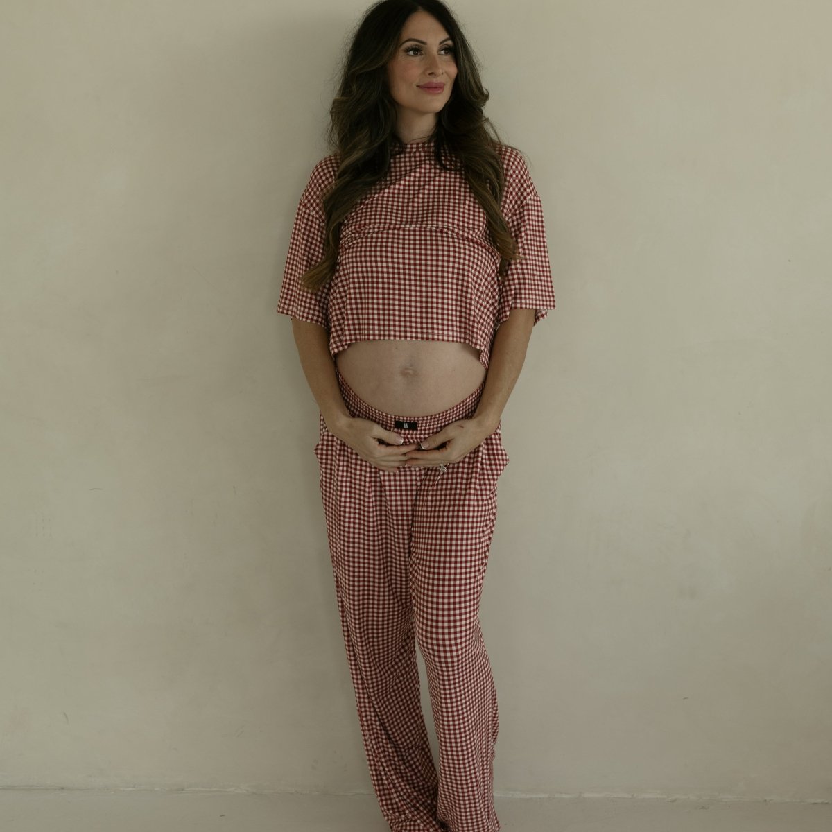 Pregnant woman wearing a red checkered outfit against a plain background