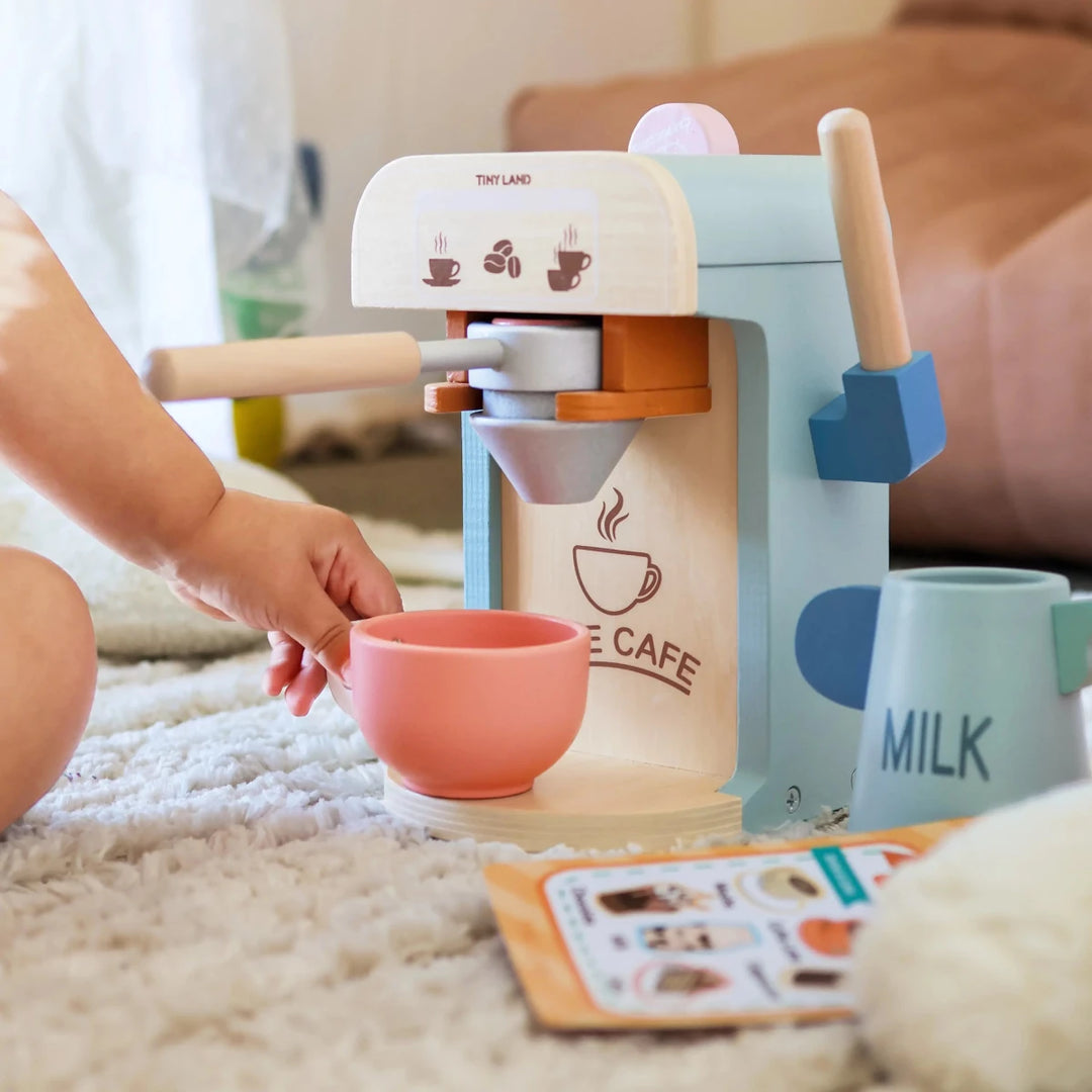 Children's toy coffee machine with a pink cup on a carpeted floor.