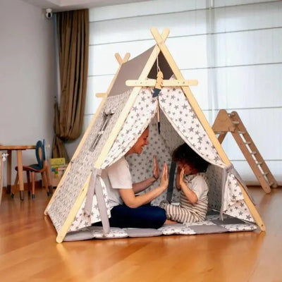 Two children playing inside a wooden teepee with star-patterned fabric in a room.